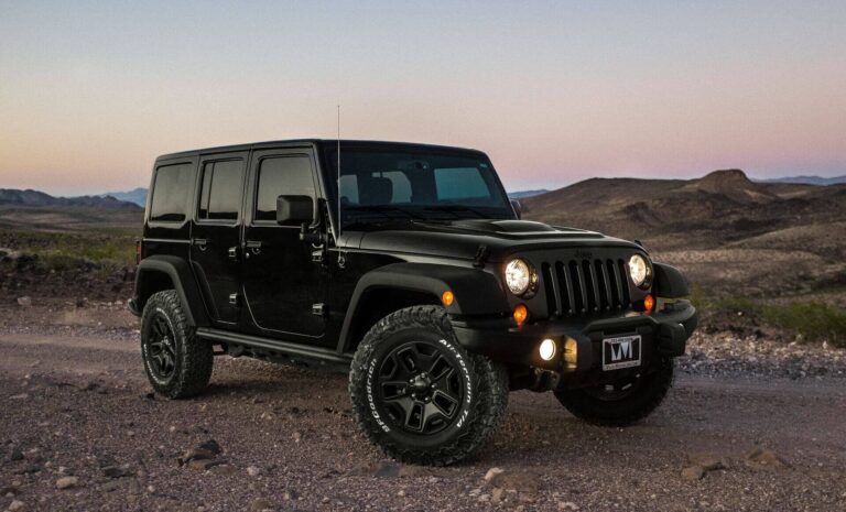 A black Jeep Wrangler on a dirt road at sunset.